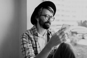 bearded man in bright checkered shirt installing new mobile application  on smartphone device and listening music. Hipster style. photo