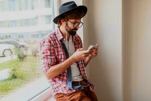 Stylish  bearded man in bright checkered shirt installing new mobile application  on smartphone device and listening music. Hipster style. photo