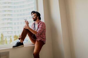 Stylish  bearded man in bright checkered shirt installing new mobile application  on smartphone device and listening music. Hipster style. photo