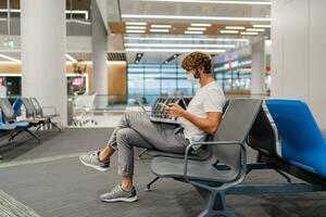 New normal and social distance concept. Man tourist wearing mask using laptop computer searching airline flight status and sitting with distance during corona virus. photo