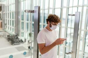 Man wearing face mask  in airport and   using smartphone . Health and travel concepts during coronavirus pandemic. photo