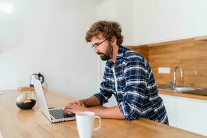 hermoso hombre persona de libre dedicación utilizando ordenador portátil estudiando en línea trabajando desde hogar, contento casual chico mecanografía en ordenador personal cuaderno surf Internet mirando a pantalla disfrutando distante trabajo sentar a mesa. foto