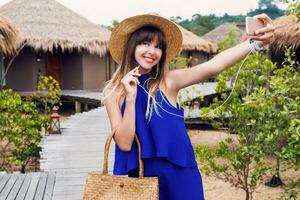 Sunny summer portrait of cute brunette woman in straw hat and trendy  boho bag walking in tropical villa in Thailand. photo