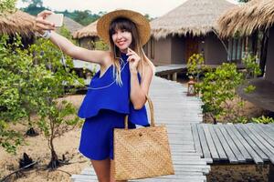 Sunny summer portrait of cute brunette woman in straw hat and trendy  boho bag walking in tropical villa in Thailand. photo