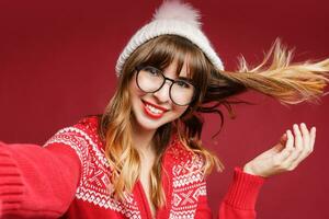 sonriente mujer en invierno atuendo posando en estudio en rojo antecedentes. foto