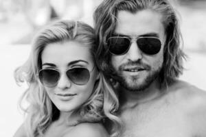 cerca arriba Moda retrato de atractivo Pareja . joven personas vistiendo Gafas de sol anteojos atlético hermoso hombre y joven bonito mujer sonriente y disfrutar verano. en negro y blanco. foto