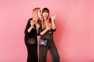 chisme muchachas con lentes de alcohol bebidas posando en ligero rosado antecedentes. fiesta humor. vistiendo lujo lentejuelas vestir . foto