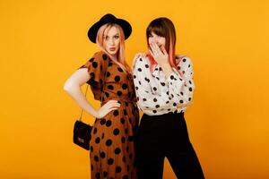 Fashionable studio shot of two stylish women with pink hairs posing over yellow background.  Ecstatic emotions. Shopping and friendship concept. photo