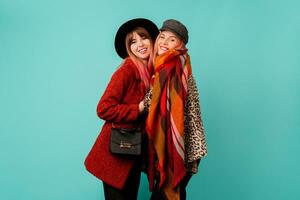 Two stylish blond  women posing in studio on blue turquoise background. Friends hugging and having fun together.  Wearing leopard print faux fur coat and wool scarf. Winter fashion. photo