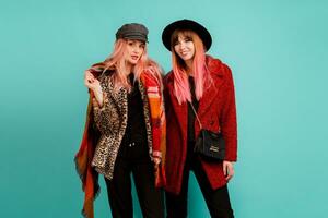 Two stylish blond  women posing in studio on blue turquoise background. Friends hugging and having fun together.  Wearing leopard print faux fur coat and wool scarf. Winter fashion. photo