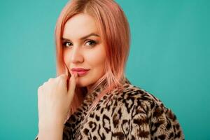 estudio belleza retrato de maravilloso mujer con rosado pelos en elegante invierno mullido Saco con leopardo impresión en vívido turquesa antecedentes. foto