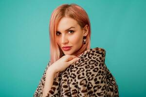 Close up studio portrait of stunning woman with pink hairs in stylish winter fluffy  coat with leopard print on  vivid   turquoise  background. photo