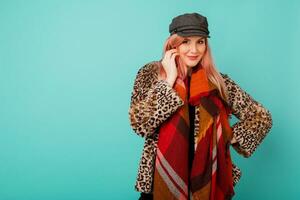 studio fashion portrait of gorgeous woman in stylish winter fluffy  coat with leopard print  playing with scarf and  posing on vivid turquoise  background. photo