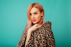 Close up studio portrait of stunning woman with pink hairs in stylish winter fluffy  coat with leopard print on  vivid   turquoise  background. photo