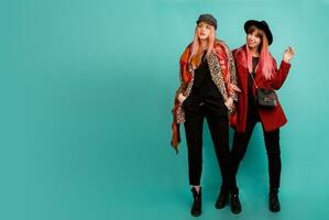 Full height image of two happy cheeky girls , best friends posing  on blue background. Wearing stylish casual   fur coat with leopard print  and hat. Space for text. photo