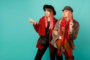 Fashionable studio shot of two stylish  models in bright winter or autumn   outfit, hat and scarf posing in turquoise  background. photo