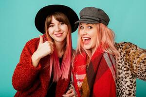 Close up studio portrait of two pretty cute models with pink hairs in stylish leopard print faux fur coat and trendy hat on turquoise. Surprise face. Winter fashionable outfit. photo