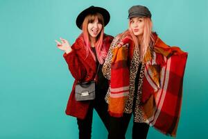 Two stylish blond  women posing in studio on blue turquoise background. Friends hugging and having fun together.  Wearing leopard print faux fur coat and wool scarf. Winter fashion. photo