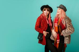 Two beautiful white women  in stylish leopard print faux fur coat and wool scarf posing on turquoise background. Fashionable winter outfit. Studio shot. photo