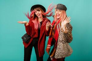 Two beautiful white women  in stylish leopard print faux fur coat and wool scarf posing on turquoise background. Fashionable winter outfit. Studio shot. photo