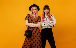 Indoor studio image of two stylish elegant females in dress posing over yellow background. Glad female models in stylish clothes. Shopping and fashion concept. photo