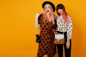 Pretty girls walking and having fun on yellow background in studio. Happy woman with pink hairs  with her blond friend  having great time. photo