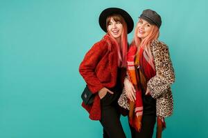 Two elegant white women  in stylish leopard print faux fur coat and wool scarf posing on turquoise background. Fashionable winter outfit. Studio shot. photo