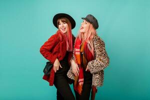 Two beautiful white women  in stylish leopard print faux fur coat and wool scarf posing on turquoise background. Fashionable winter outfit. Studio shot. photo