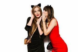 Two happy attractive young  women, funny cute friends  drinking vine and having fun over white background. Two girls cerebrating  new  year, birthday party. Wearing elegant evening red  dress. photo