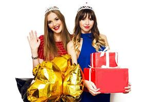 Friends party. Two attractive  women  holding gift boxes and gold shaped star balloons in masquerade crowns  on white background. photo