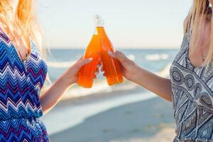 verano Días festivos y vacaciones concepto. amigos Bebiendo limonada o alcohol , participación bebida en botellas disfrutando puesta de sol en el playa. fiesta tiempo. atención en botella. foto