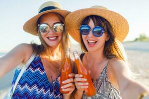 Summer holidays and vacation concept.  Friends drinking lemonade  or alcohol , holding beverage in bottles. Enjoying sunset on the beach. Party time. Focus on bottle. photo