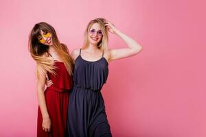 Two  carefree female having fun and dancing  on pink background. Flash portrait. Party mood . Similar dress. Friendship concept. photo