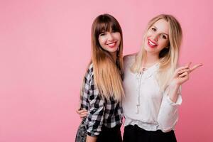 Two smiling women hugging and standing isolate over pink background . Brunette and blonde girls. Natural make up. photo