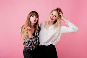 Two smiling women hugging and standing isolate over pink background . Brunette and blonde girls. Natural make up. photo