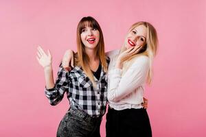 Two smiling women hugging and standing isolate over pink background . Brunette and blonde girls. Natural make up. photo