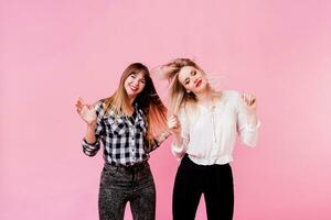 Two carefree female having fun and dancing on pink background. Flash portrait. Party mood . Friendship concept. photo