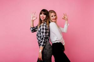 Great team, two successful colleagues  posing over pink background and  showing signs. photo