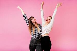 Two exited woman having fun and  raising hands up.  Standing on pink background.  Lucky  mood. photo