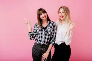 Two smiling women hugging and standing isolate over pink background . Brunette and blonde girls. Natural make up. photo