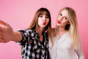 Two funny women making self portrait on pink background. photo