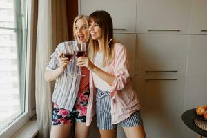 Couple of happy carefree women looking at window and holding glass of wine. Cozy home atmosphere. photo