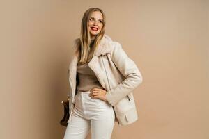 Winter studio fashion photo of elegant blond woman with red lips wearing trendy eco leather jacket , posing over beige background.