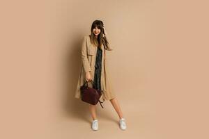 Stylish brunette woman  wearing trendy coat  , posing over beige background.  Winter fashion trends. photo