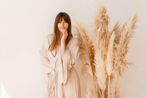 Elegant woman in stylish bohemian silk kimono posing over white background in studio with pampas grass decor. photo