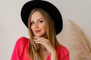 Close up  portrait   blond woman in black hat and ink dress posing in studio  in studio with pampas grass decor. photo