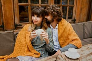 Romantic moments. Chilling couple in love sitting on terrace  and drinking morning coffee and enjoying  breakfast.  Man and woman covered by blanket. photo
