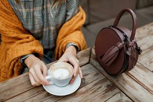 Woman drinking coffee . Stylish bag on table. Wearing grey dress and  orange plaid. Enjoying cozy morning in cafe. photo