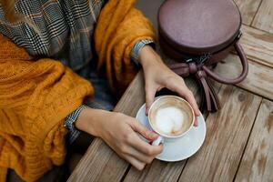 Woman drinking coffee . Stylish bag on table. Wearing grey dress and  orange plaid. Enjoying cozy morning in cafe. photo