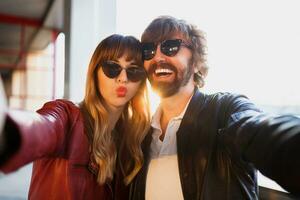 Happy beautiful stylish couple of love making self portrait by camera, walking in modern city. Perfect smile, leather jacket.  Fashionable outfit. photo